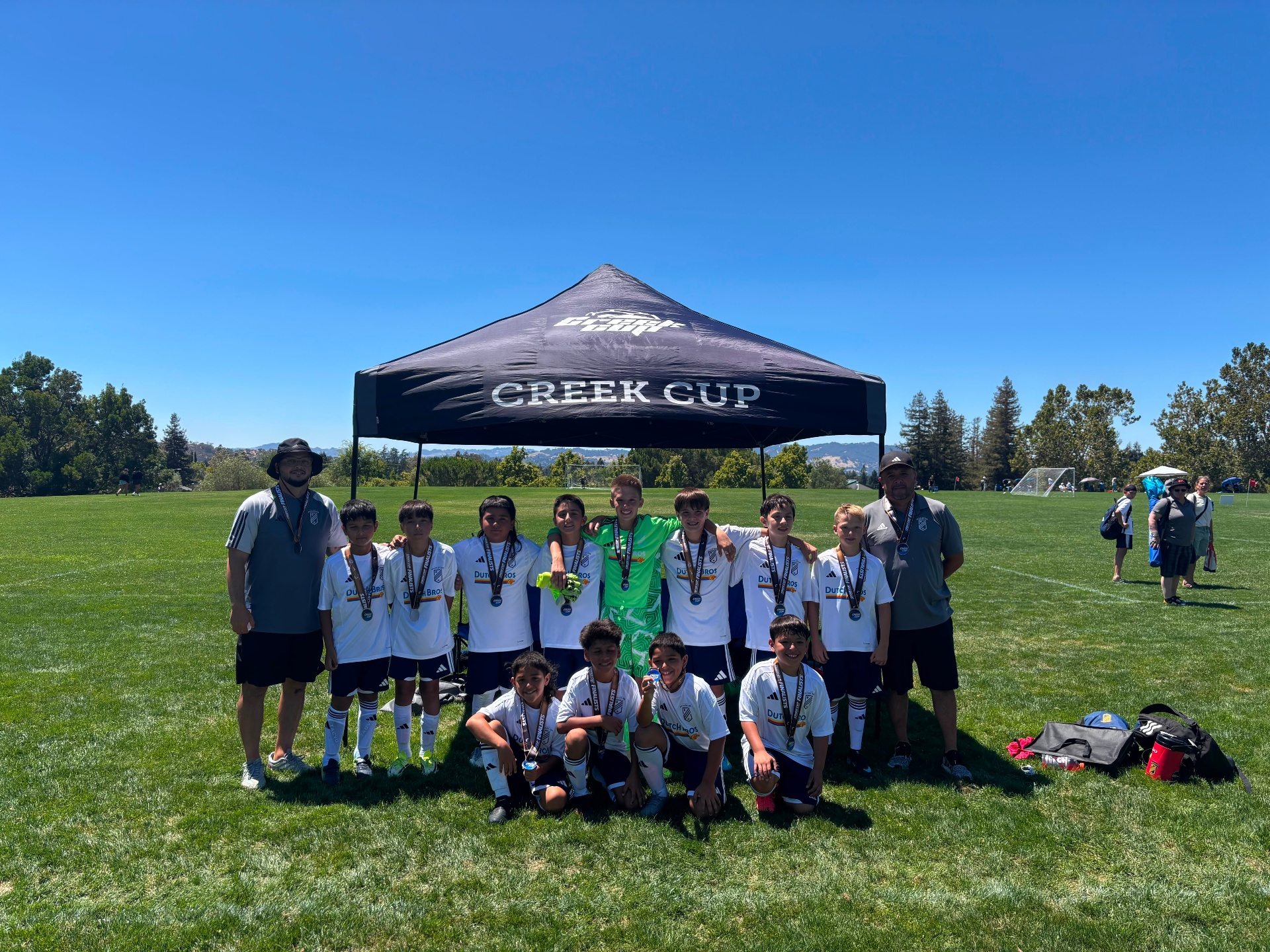 EC Revolution U11 Boys Blue players and coaches with their Creek Cup finalist medals under the Creek Cup tent
